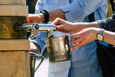 Midsection of woman filling water metal container outdoors