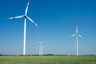 Windmills on field against clear blue sky