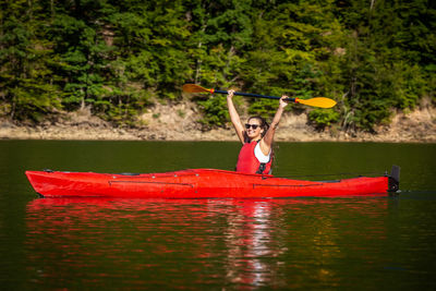 Man holding red boat in lake against trees