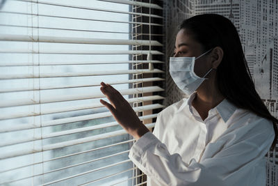 Portrait of a young woman standing against window