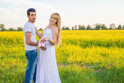 Portrait of couple holding baby shoes while standing on field