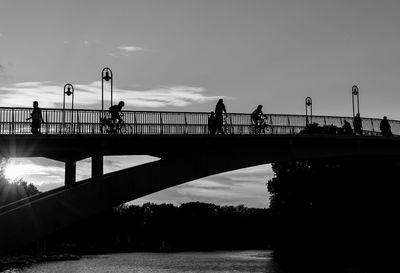 Silhouette people on bridge over river against sky