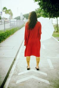 Rear view of woman holding umbrella while standing on footpath