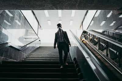 Rear view of man walking on escalator