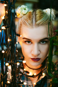 Close-up portrait of young woman holding illuminated string lights and lantern at home