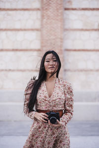 Woman with analog camera standing by wall