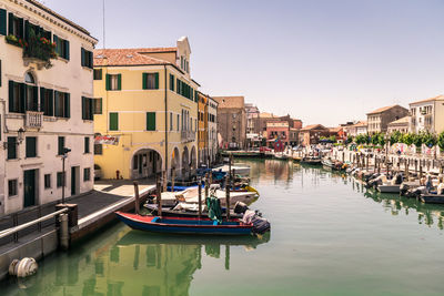 Boats moored in canal by buildings against sky in city