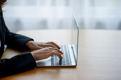 Cropped hands of woman using laptop on table at home