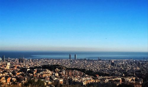 High angle view of townscape by sea against clear blue sky