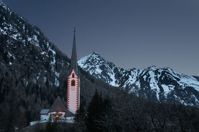 Church by snowcapped mountains against clear sky during winter