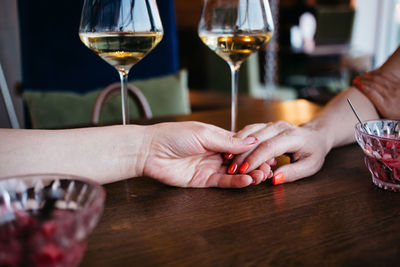 Women hold each other's hands, close up hands, restaurant table, romantic dinner, wine, celebration