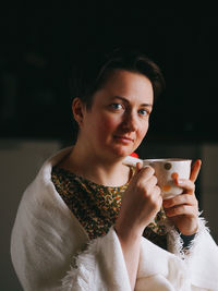 Portrait of a young woman with short hair at home with a cup of coffee or tea in the evening.