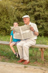 Grandfather reading newspaper while sitting by grandson in park