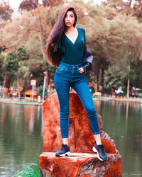 Portrait of woman standing by lake against trees