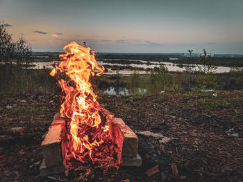 Bonfire on log against sky during sunset