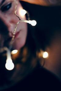 Close-up of woman with illuminated string lights