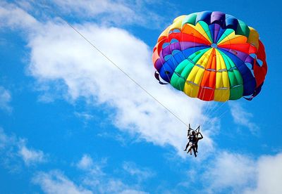 Low angle view of people parasailing against blue sky on sunny day