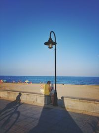 People sitting on beach against clear blue sky