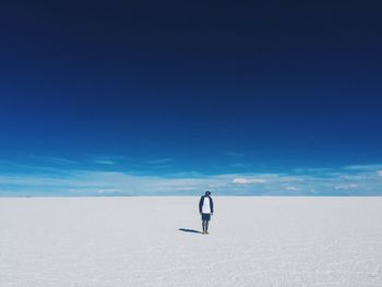 Man standing at salar de uyuni against blue sky