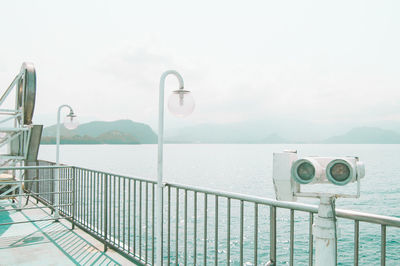 Metal railing by sea against sky