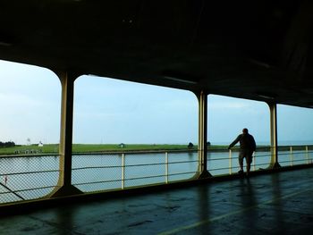 Silhouette man standing by railing against sky