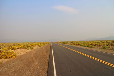 Empty road amidst field against sky on sunny day