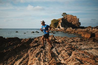 Full length of man running on rocks at beach against sky