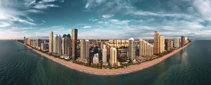 Panoramic view of modern buildings by sea against sky