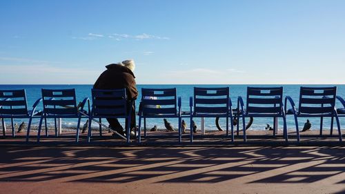 Rear view of man on chair at beach against sky