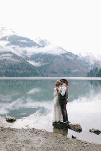 Two happy people in love the bride and groom in wedding outfits embrace by the lake and mountains