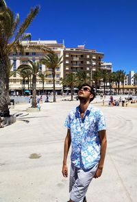 Young man standing against blue sky in city