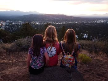 Rear view of women sitting on mountain looking at sunset