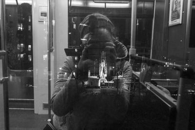 Rear view of man photographing through window at night