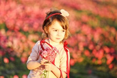 Portrait of cute girl standing against red flowering plants