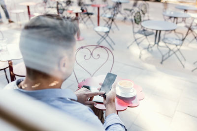 Businessman using smart phone at sidewalk cafe seen through glass window