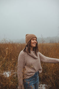 Woman wearing hat standing on field against sky during winter