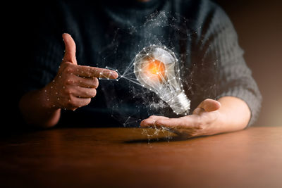 Digital composite image of hands by illuminated light bulb on table