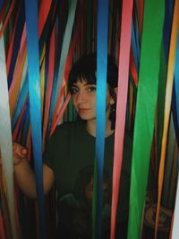 Portrait of young man standing against multi colored curtain