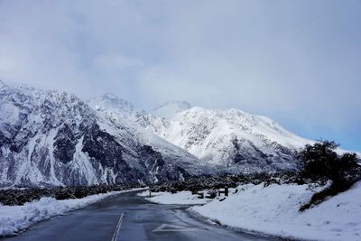 Snow covered road by snowcapped mountain against sky