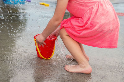 Little child playing with water and toy bucket at splash pad in the local public park in summer 