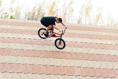 Full body man in casual clothes doing wallride trick on bmx bicycle on slope on summer weekend day in skate park