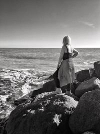 Rear view of woman standing on beach against clear sky