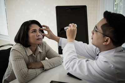 Doctor examining woman while sitting at table in hospital