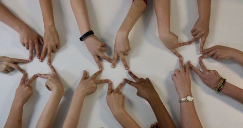 Cropped hands of friends forming star shapes with fingers on white table