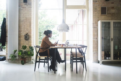 Female architect using phone while sitting by table at home