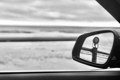 Close-up of side-view mirror against sky