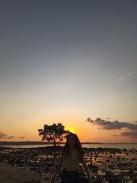 Woman standing on beach against sky during sunset