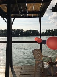 Empty chairs by river against sky