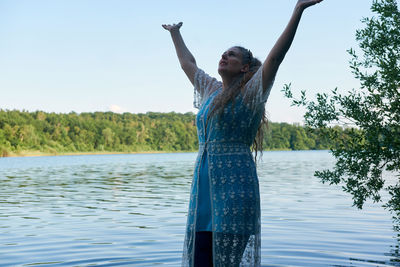 Woman standing by tree in lake against sky