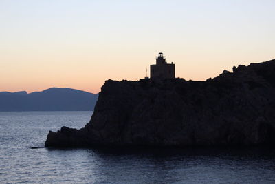 Lighthouse by sea against sky during sunset